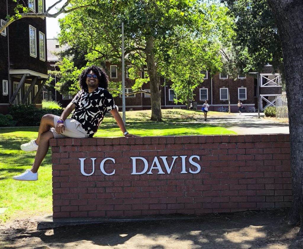 Vitor Gonçalves da Silvia sentado em muro que diz "UC Davis"